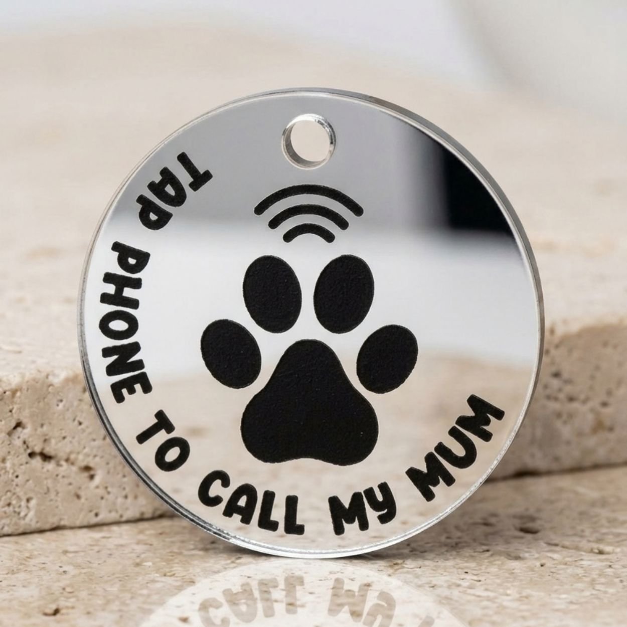 Close-up of a silver NFC pet tag with paw print and tap phone to call my mum text